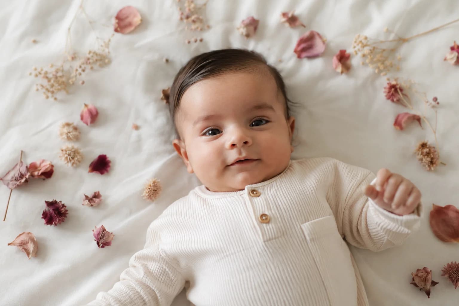 Baby boy lying on white cotton surrounded by dried flowers and pink rose petals