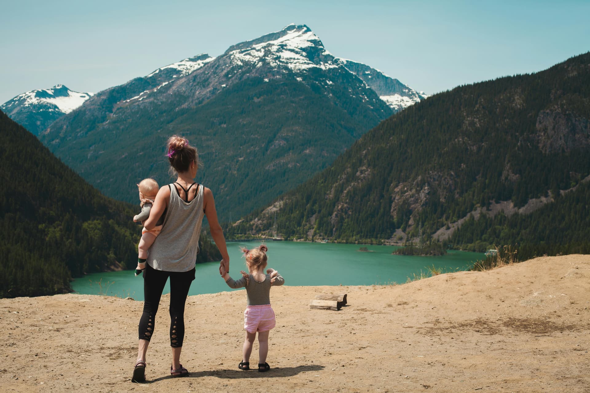 Family standing on a viewpoint above a turquoise lake with forested mountains and snow covered peaks in the background.